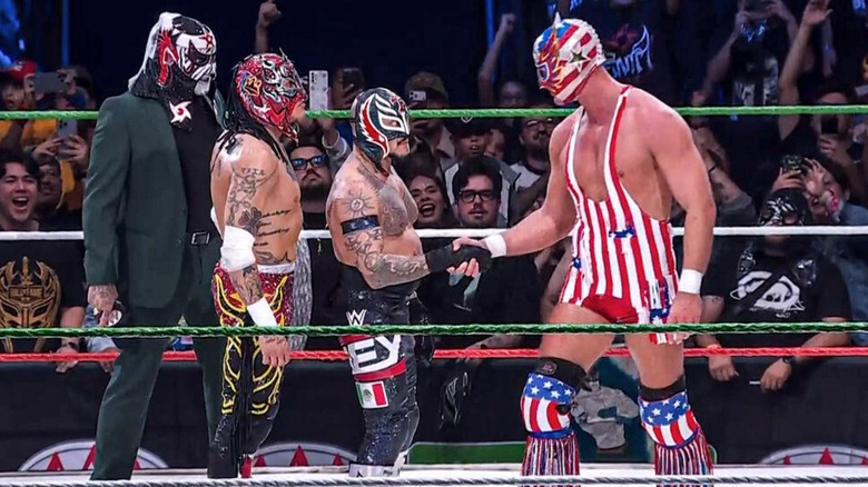 Penta and Rey Fenix watching on as Rey Mysterio and El Grande Americano shake hands following their match at AAA Guerra de Titanes 2025.