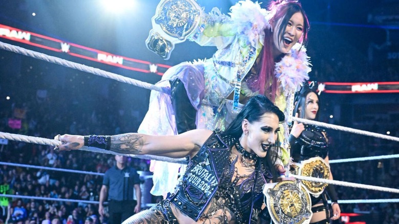 IYO SKY and Rhea Ripley pose with the WWE Women's Tag Team Championships on the ropes, flanked by Stephanie Vaquer, before a match on 