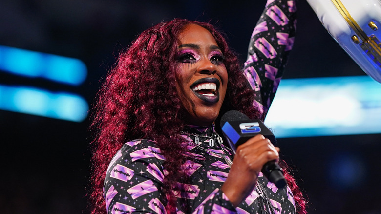 Naomi holding a WWE SmackDown mic and the Money in the Bank briefcase