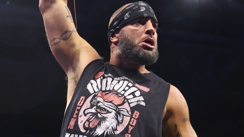 Mark Briscoe raises right arm wearing black sleeveless shirt.