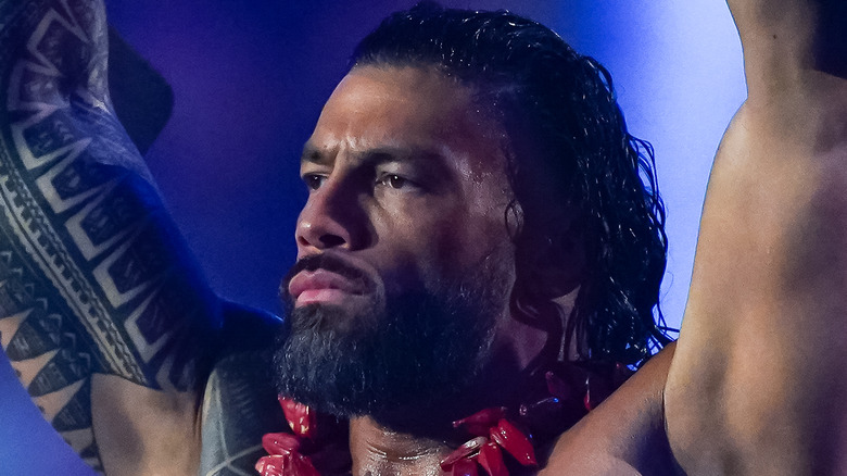 Roman Reigns holds his title belts high