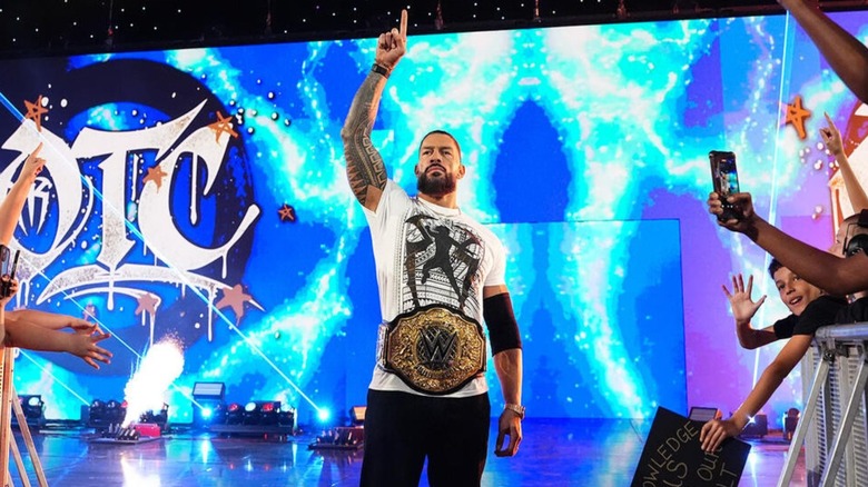 Roman Reigns poses on the stage, World Heavyweight Championship around his waist, before a contract signing segment on 