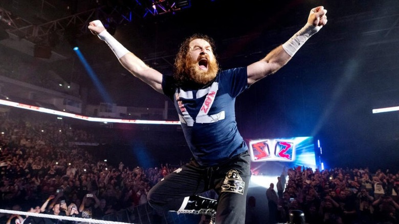 Sami Zayn poses and cheers, standing on the turnbuckle in the ring, before a match on WWE TV.