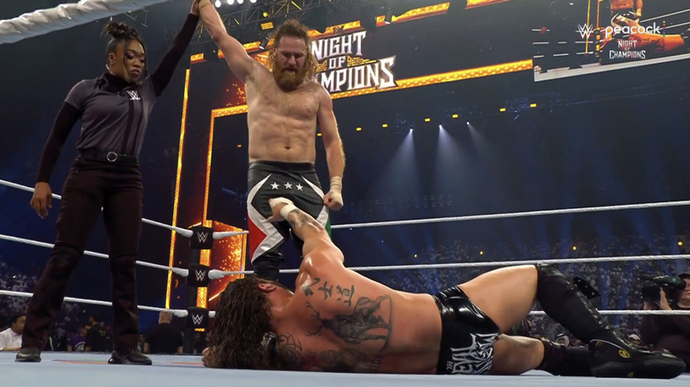 Sami Zayn has his hand raised as he looks down on a grounded Kross.