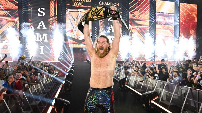 Sami Zayn holds up his newly-won Undisputed WWE Championship on the ramp as pyro goes off behind him following his victory at WWE Night of Champions 2026.