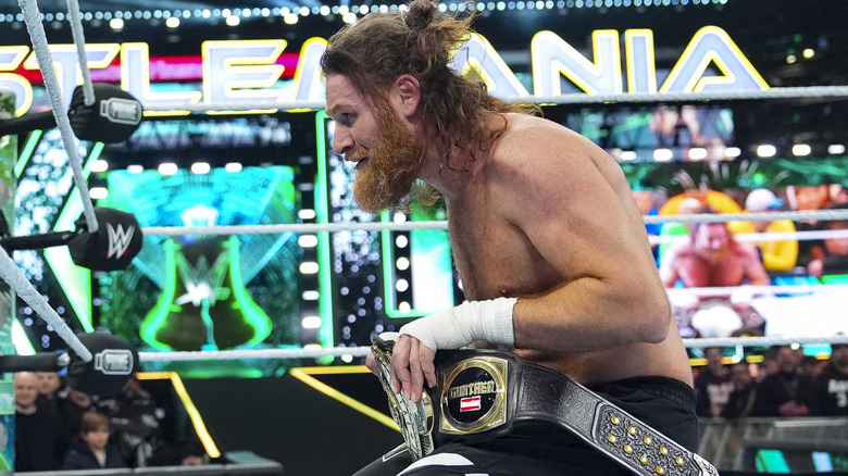 Sami Zayn kneeling in wrestling ring with WWE intercontinental title