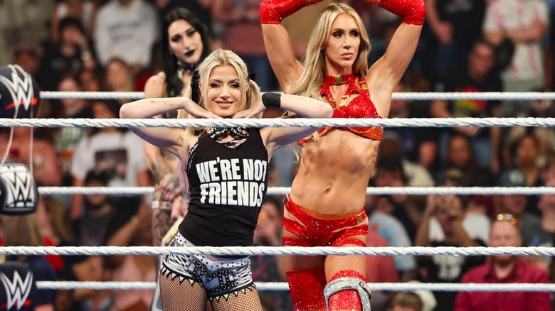 Charlotte Flair and Alexa Bliss pose in the ring before a tag team match alongside Rhea Ripley on 