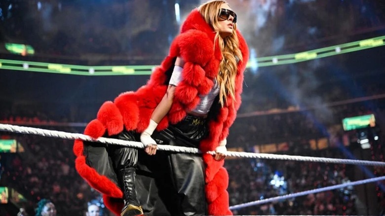 Becky Lynch poses on the ropes, wearing a big, puffy red coat, before a segment on an episode of 