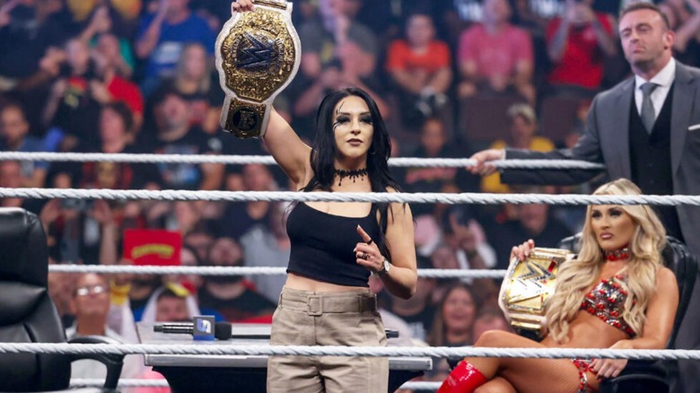 Stephanie Vaquer holding the Women's World Championship out towards the crowd while Nick Aldis and Tiffany Stratton are in the background.