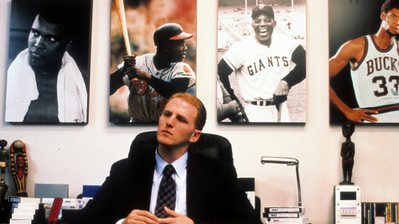 Michael Rappaport sits at a desk in "Bamboozled," with pictures of black athletes behind him.