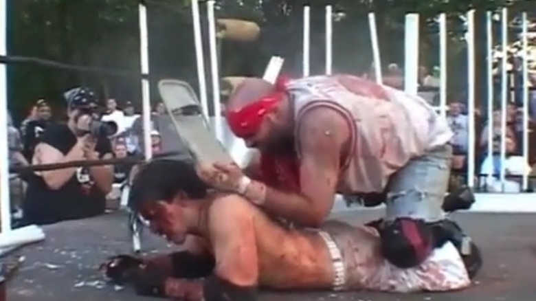 Nick Gage kneels on Thumbtack Jack