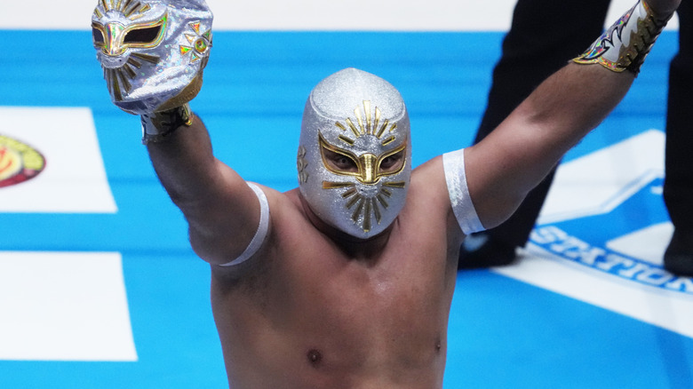 Mistico, a masked luchador, holding up another mask