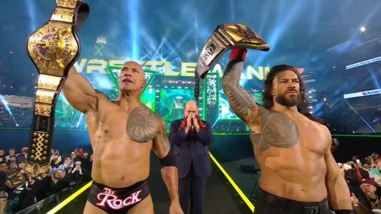 The Rock and Roman Reigns holding up title belts
