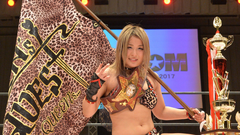 Io Shirai poses with a trophy and flag in the ring following a tournament victory in Stardom.