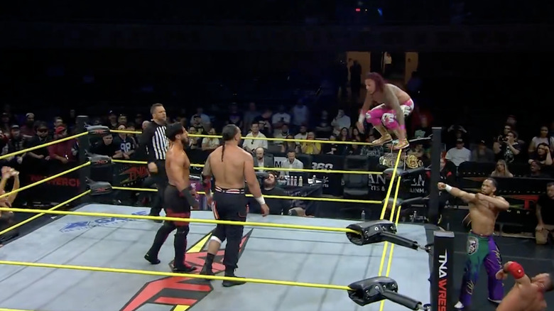 Navarro on the top rope as Ali and Santana stand in the ring and several other competitors are on the outside