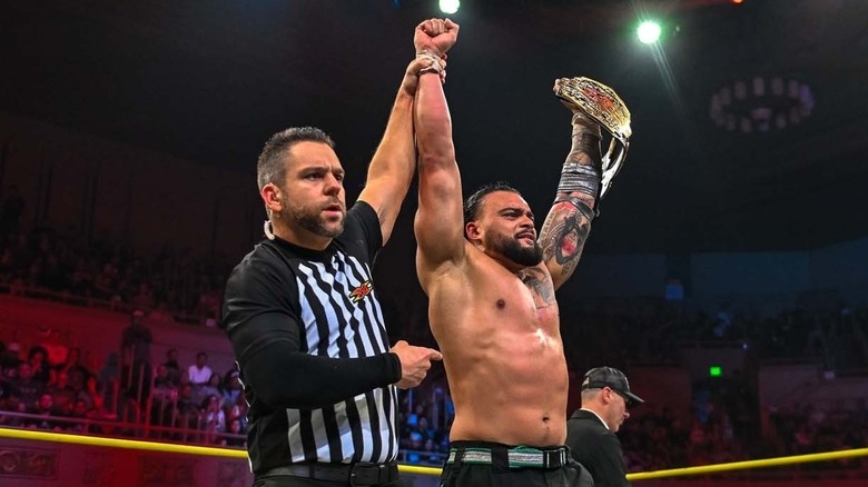 Referee holding up Mike Santana's arm as he holds world title