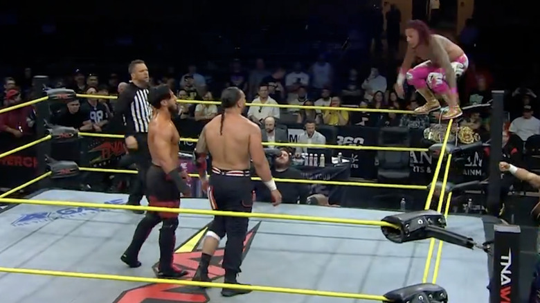 Navarro on the top rope as Ali and Santana stand in the ring and several other competitors are on the outside