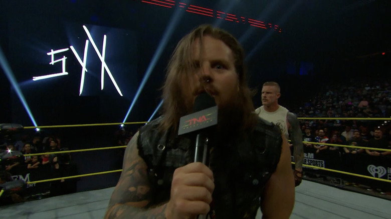 Gacy leaning towards the camera as Shaw stands behind him