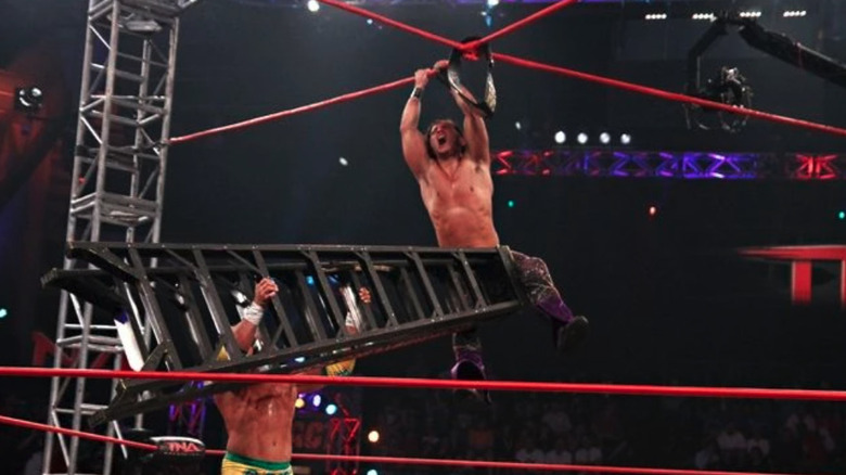 A member of Generation Me hangs from the X while Robbie E holds a ladder beneath him at TNA Victory Road 2011