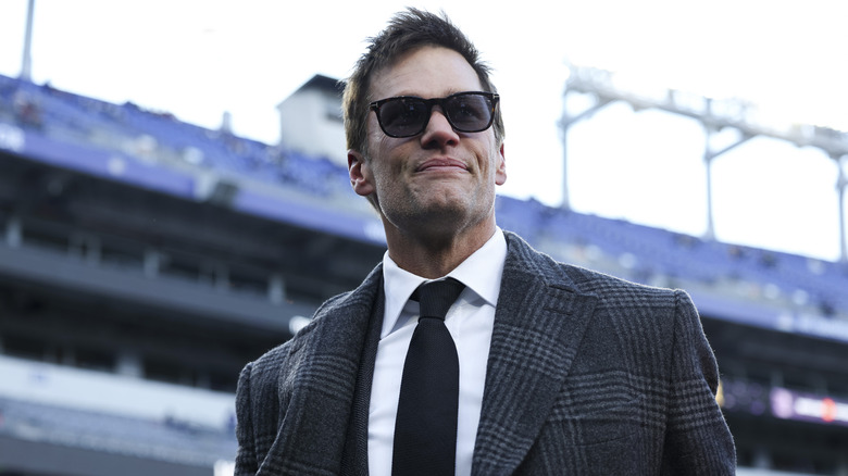 Tom Brady smiles on while watching a Patriots game on the sidelines