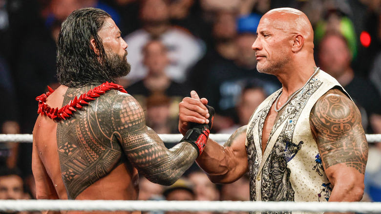 Roman Reigns and The Rock (The Head of their family's tables) exchange a handshake.