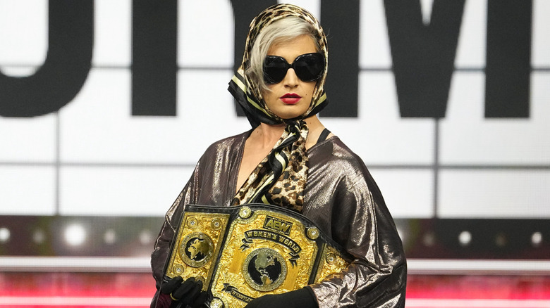 Toni Storm poses with the AEW Women's World Championship on the stage, wearing sunglasses and a scarf, during an episode of 