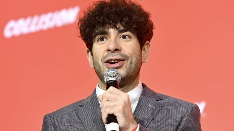 Tony Khan speaks into the microphone he holds near his mouth.