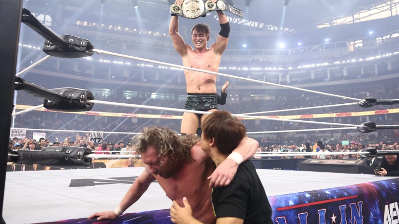 Kazuchika Okada holding the AEW Unified Championship above his head mocking Kenny Omega and Kota Ibushi after defeating the former at AEW All In: Texas, 2025.