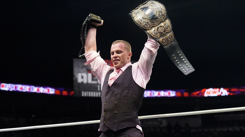 Kyle Fletcher holds up his TNT Championship and the AEW World Championship while standing over 