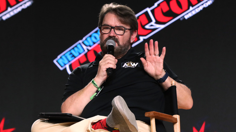 Tony Schiavone sitting down with his palm raised defensively