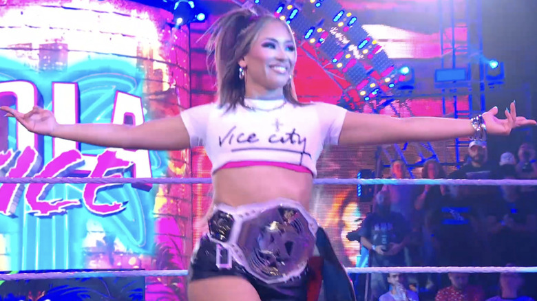 Lola Vice poses with her "NXT" Women's Championship and her AAA World Mixed Tag Team Championship