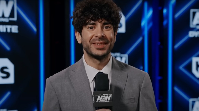 Tony Khan smiling while holding a microphone