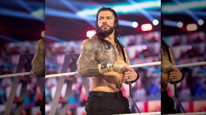 Roman Reigns de pie en el delantal del anillo con cinturón de campeonato, con guante de oro