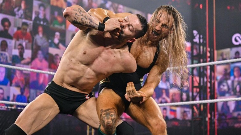 Pete Dunne applies a hold to NXT Champion Finn Balor in the middle of the ring during their match at NXT TakeOver: Vengeance Day 2021.