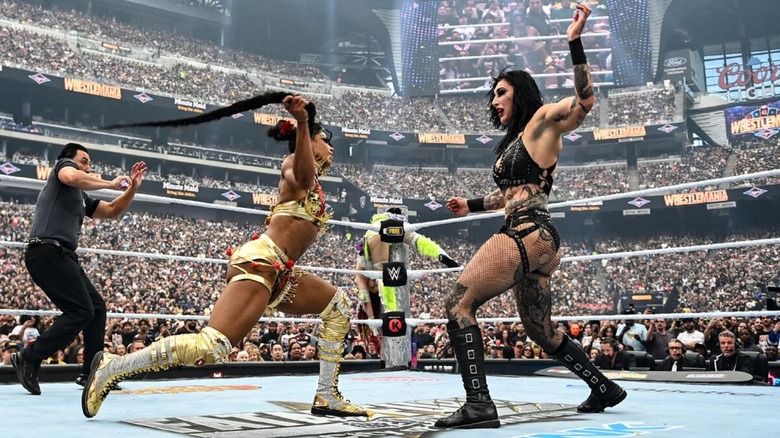 Bianca Belair looks to whip Rhea Ripley with her brain, as a referee shrinks back and IYO SKY is laid out on the top rope, during their match at WrestleMania 41.