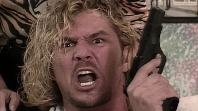 Brian Pillman holds up a gun and shouts to the camera in his home during a segment on WWF television.