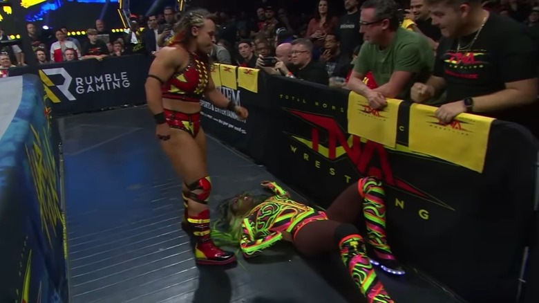 Jordynne Grace stands over a fallen Trinity on the floor, outside of the ring, as fans look on during their match at Hard to Kill 2024.