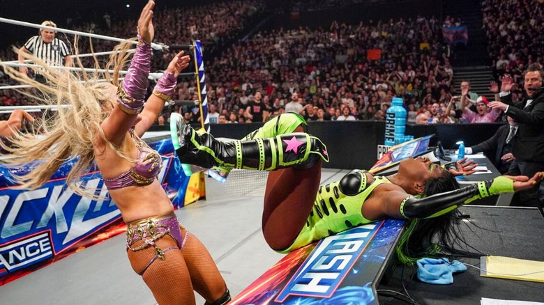 Naomi lays across the commentary desk after taking an Alabama Slam from Tiffany Stratton during their triple threat match involving Bayley at Backlash 2024.