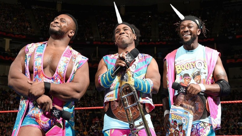 Big E, Xavier Woods, and Kofi Kingston smile in the ring, the latter stablemates wearing unicorn horns, during a promo segment on 