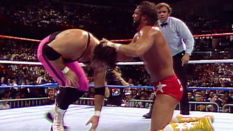 "Macho Man" Randy Savage grips the back of "The Hitman" Bret Hart's head.