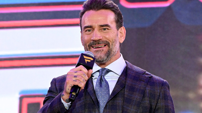 CM Punk is holding a microphone and smiling