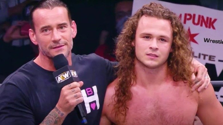 CM Punk stands in the ring with his arm around "Jungle Boy" Jack Perry on AEW TV.