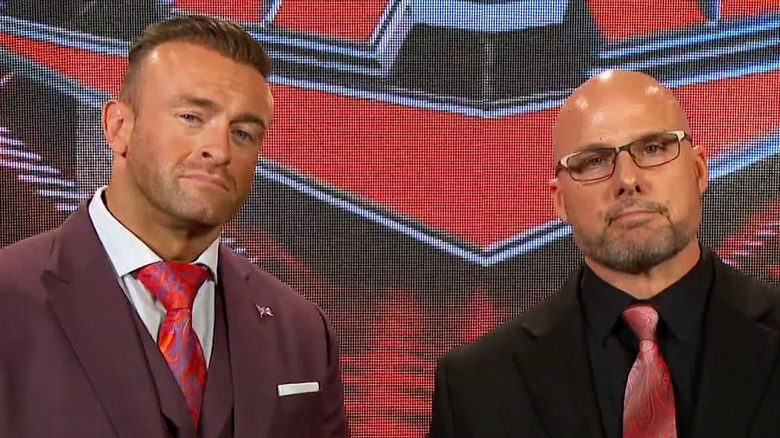 Nick Aldis standing next to Adam Pearce in front of WWE Raw logo