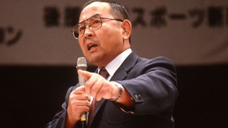 Hisashi Shinma speaks into a microphone, addressing the crowd, before an event.