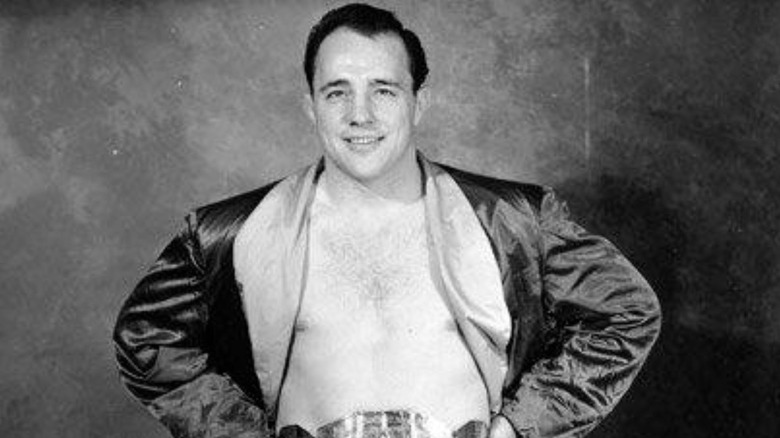 Verne Gagne poses backstage wearing a title belt in a black-and-white photo posted to WWE.com.
