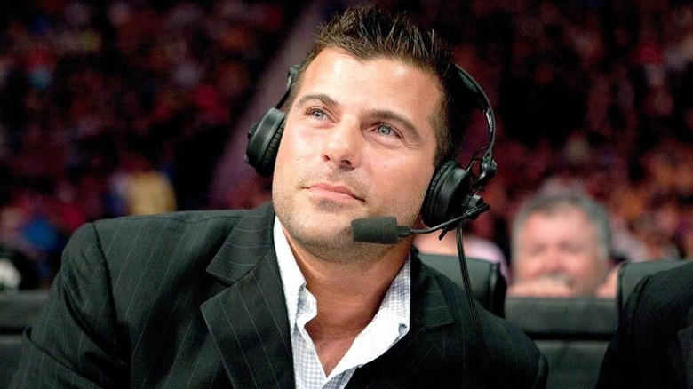 Matt Striker looks to the ring during a match while sitting at the commentary desk, wearing a headset.