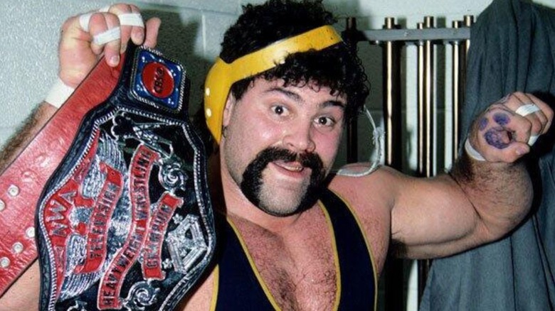 Rick Steiner, wearing a University of Michigan singlet, holds up an NWA championship in a posed photo.