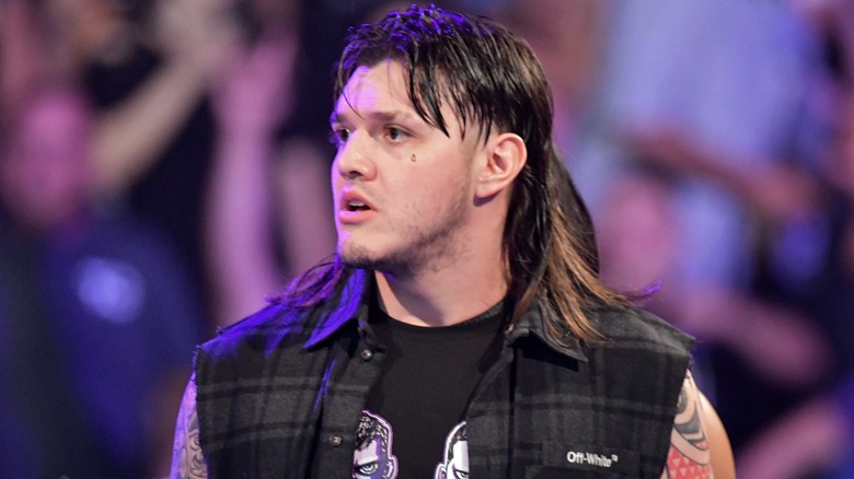 Dominik Mysterio looking confused in black flannel shirt with sleeves cut off
