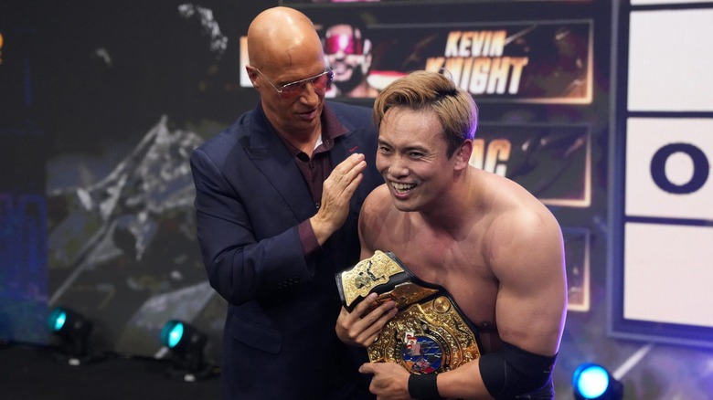 Don Callis stands alongside a grinning Kazuchika Okada as Okada holds the AEW Unified Championship.