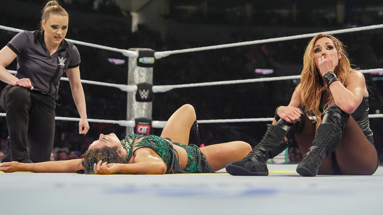 A frustrated Becky Lynch sitting beside a beaten but not broken Lyra Valkyria as the referee looks on at WWE Backlash